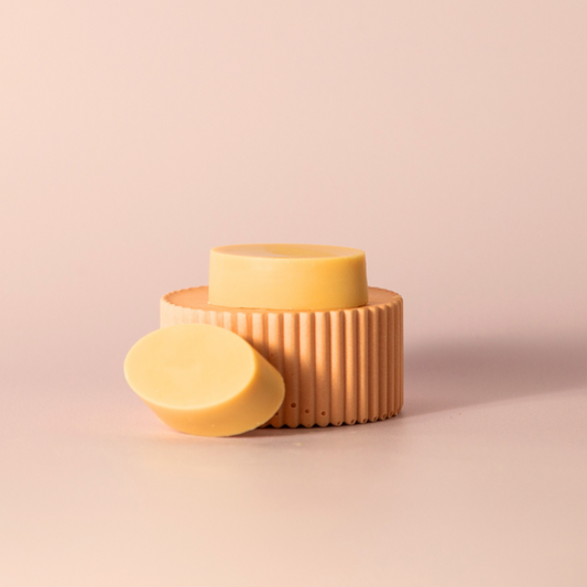 Two oval-shaped, packaging-free lip balms resembling slices of butter.