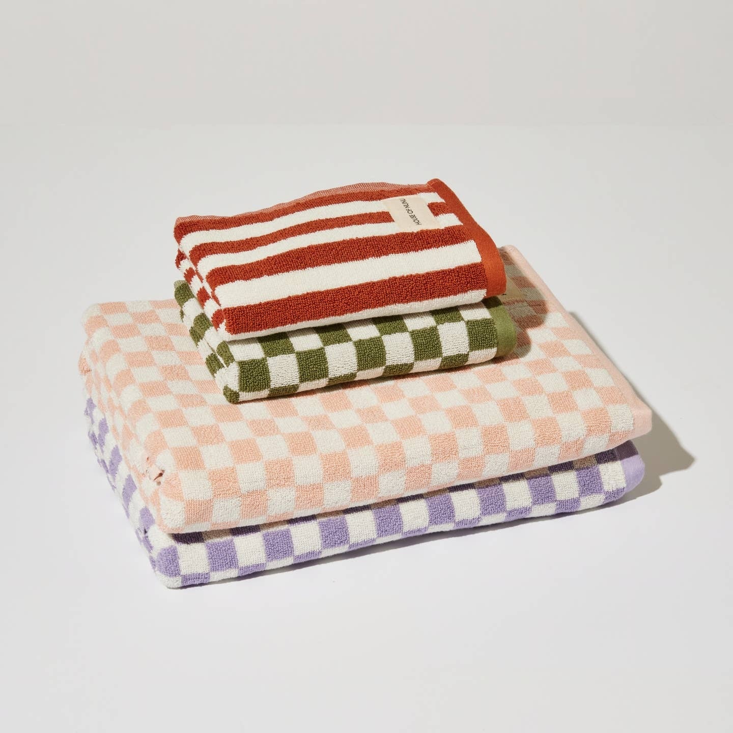 A collection of House of Nunu's check towels in a neat pile. The designs feature a forest green check, a soft peach, a lilac and finally a red stripe. 