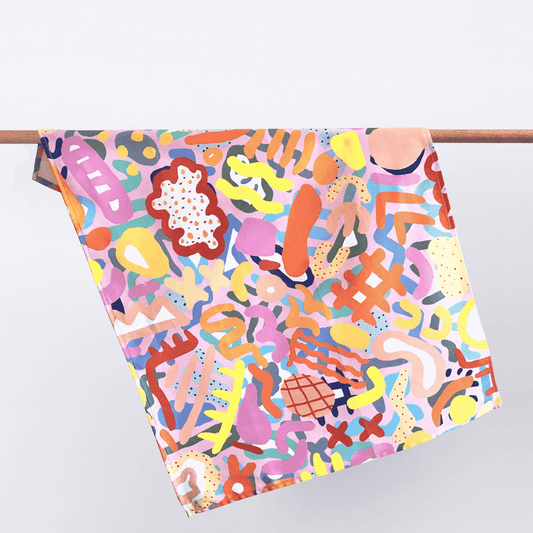 A colourful tea towel by Shuh Lee, it features a print emulating different shapes of coral in all different colours including yellow hues, bright orange, deep red and soft pastel pink.  