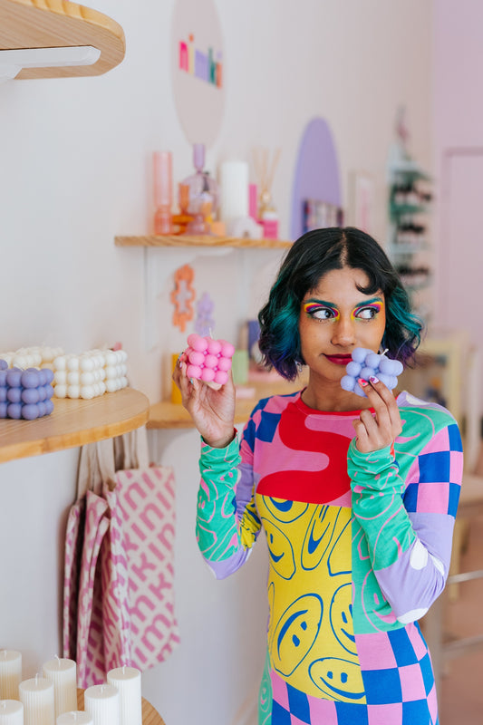 Nimki model Eishi in store holding up two bubble candles, one in pink and the other in lilac. 