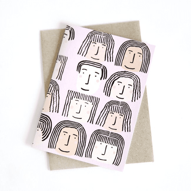 A collection of happy faces on a small greeting card by Shuh. Each face has squiggly hair and their appearance differs ever so slightly. It's playful & cheeky. 