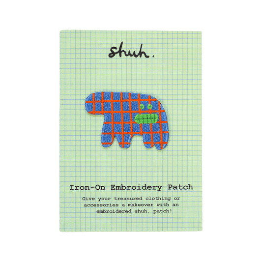 Shuh Lee Embroidery Patch: A funny abstract, surreal animal. It has four short  legs with a thick, short train. It's body is a sea blue with patchwork red lines across. It has a funny, open mouth showing its green teeth with small green eyes in the same shade. 