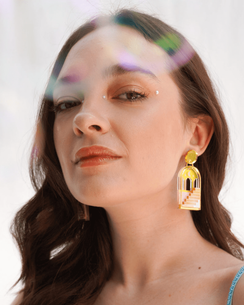 Flowatures Stairways to possibilities earrings being worn by model. The earrings are gold, pink and silver. They feature stairs leading up to golden arches with the moon and stars above. 