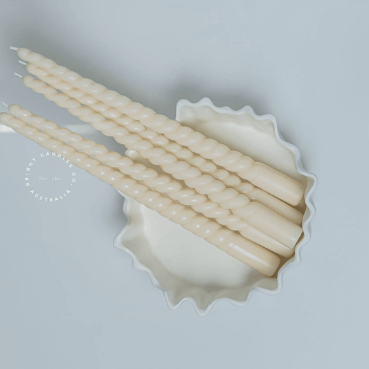 A stack of thin taper pillar candles in a white bowl. They have a soft curve running all the way through them. 