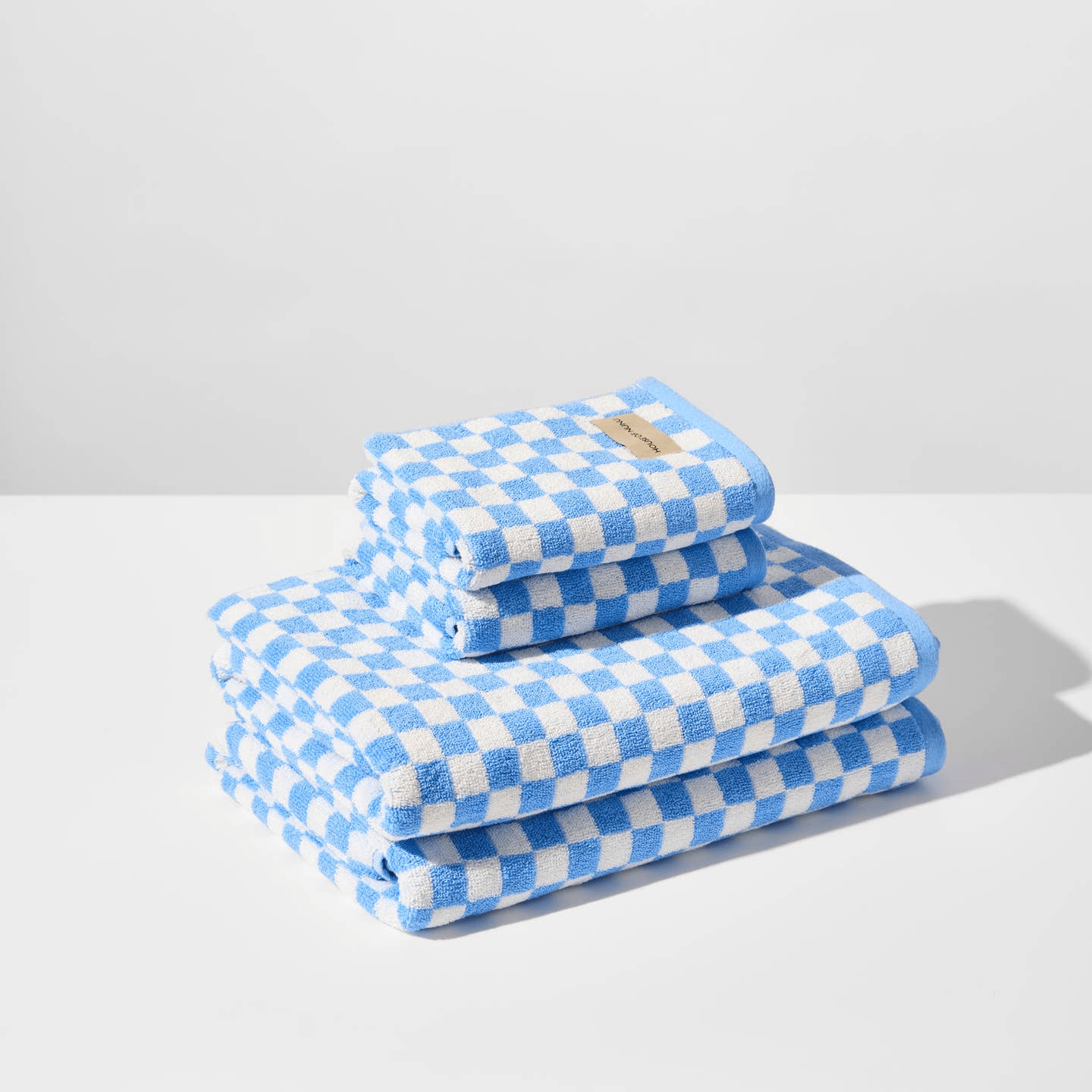 A super cute pile of bath towels and hand towels by House of Nunu: It's folded into a neat rectangle with a white base colour and light blue checks. 