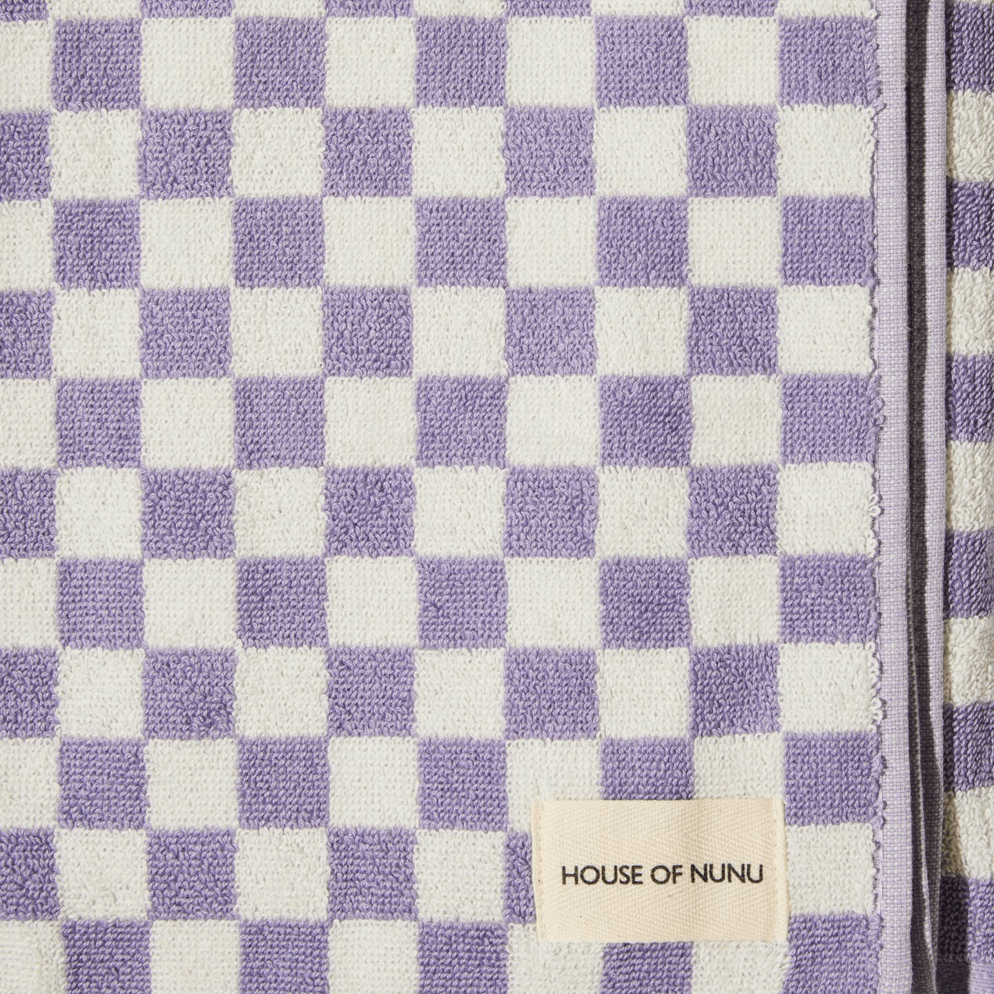 A close up shot of a cute bath towel by House of Nunu. It's folded into a perfect rectangle and features lilac checks on a white background. 