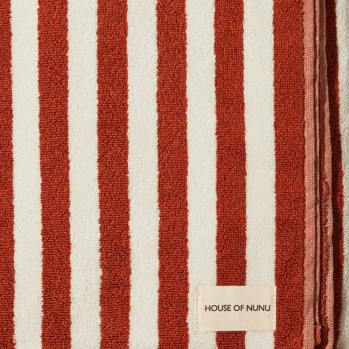 A close up of a House of Nunu hand towel with a white background and a red stripe. 