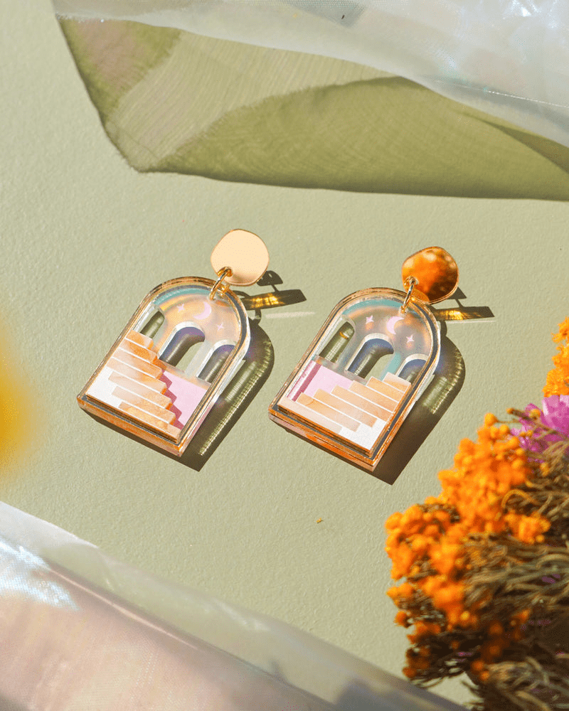 Flowature's Stairway's to possibilities Dangle earrings. The are an arch shape with a gold frame and stud at the top. Inside are smaller arches with the moon and stars above with stairways leading up to them below. 