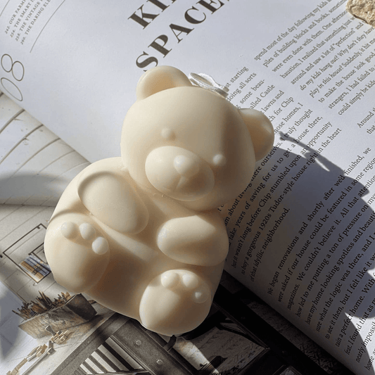 A super cute, white teddy bear candle in between the pages of a homewares magazine. 