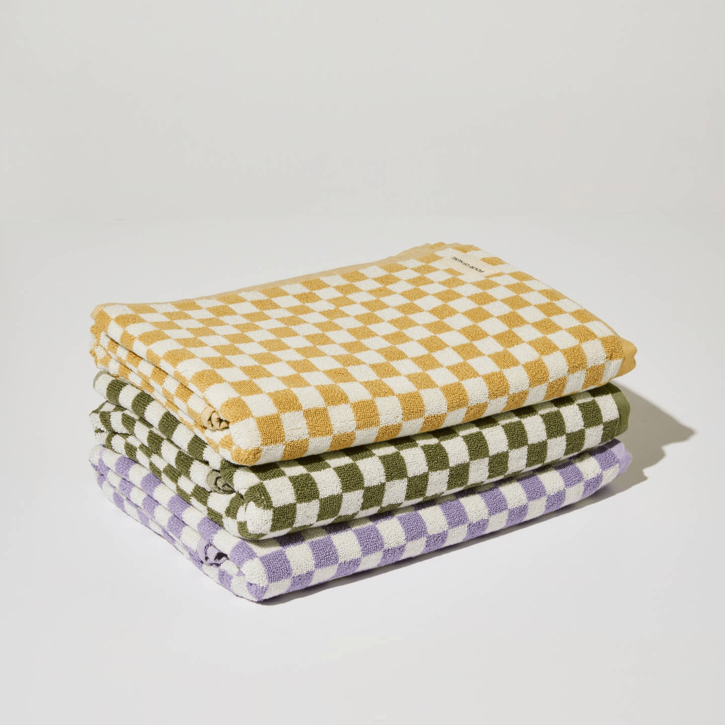 A pile of yellow, green and lilac check bath towels folded perfectly on top of each other by House of Nunu. 